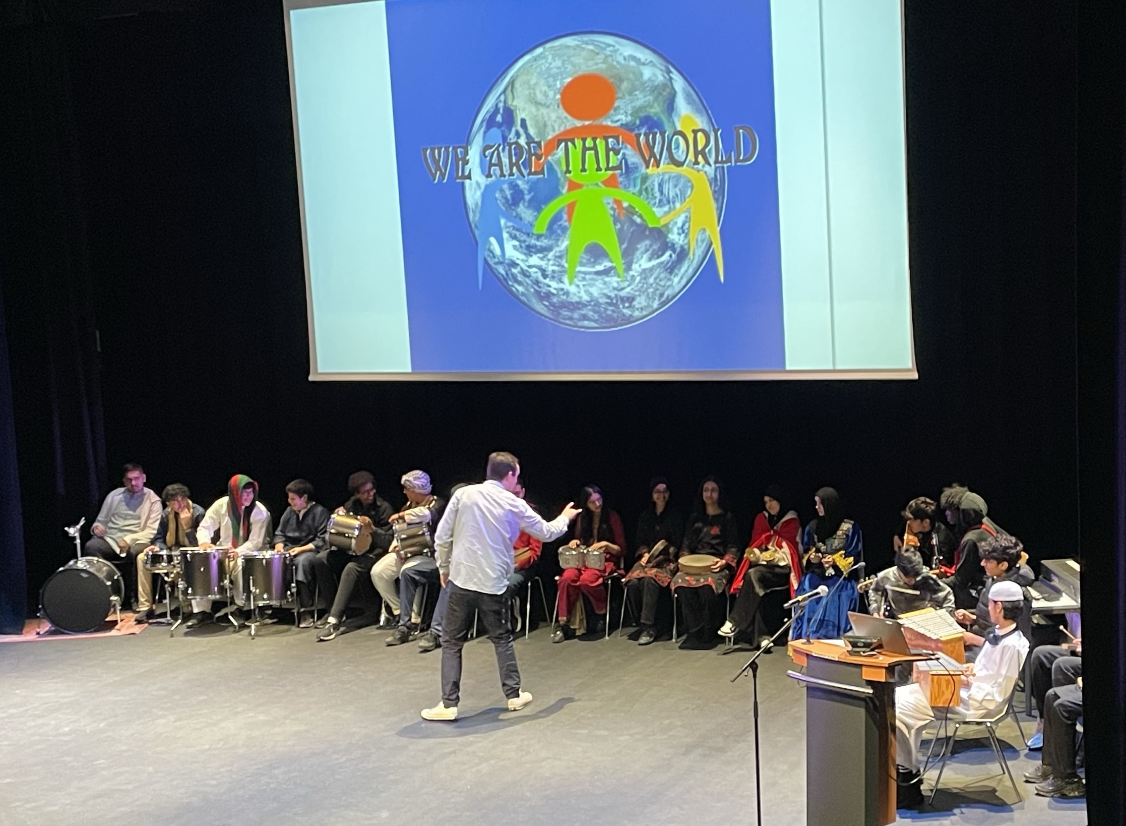 en person som står foran en stor skjerm med folk som sitter i stoler