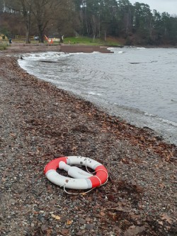En rød og hvit sko på en steinete kyst ved et vannområde