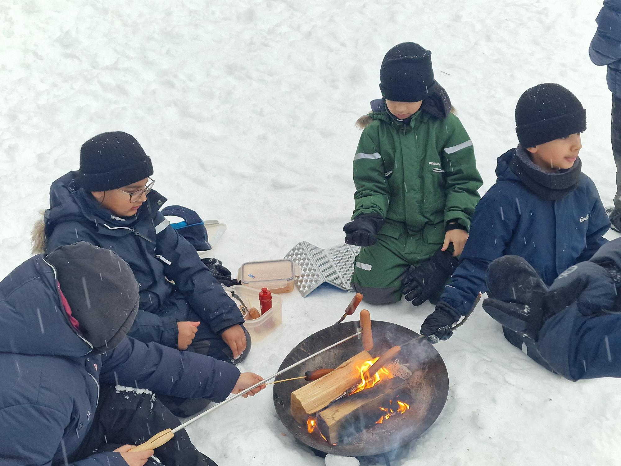 en gruppe mennesker som sitter rundt et bål i snøen